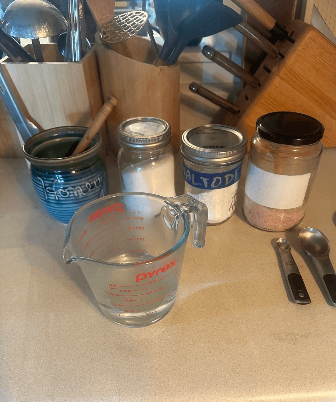 Stephanie's race-fuel ingredients on the kitchen counter: honey, table salt, maltodextrin, pink salt, and a Pyrex measuring cup of water.